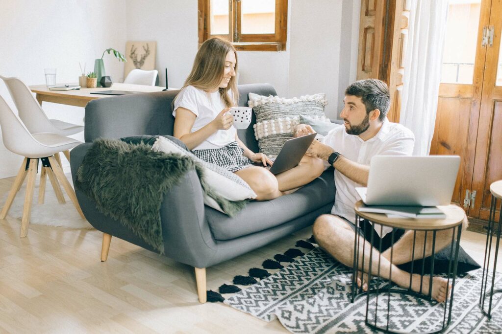 A woman sitting on a couch talking with a man on the floor while they make their wedding guest list