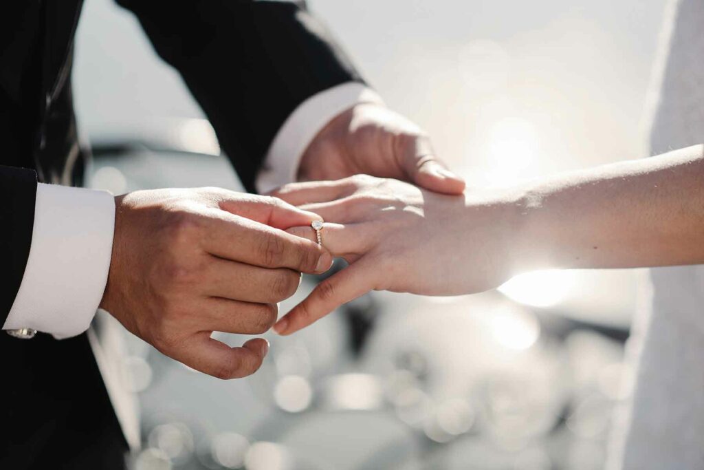A man sliding a wedding ring onto an outstretched finger