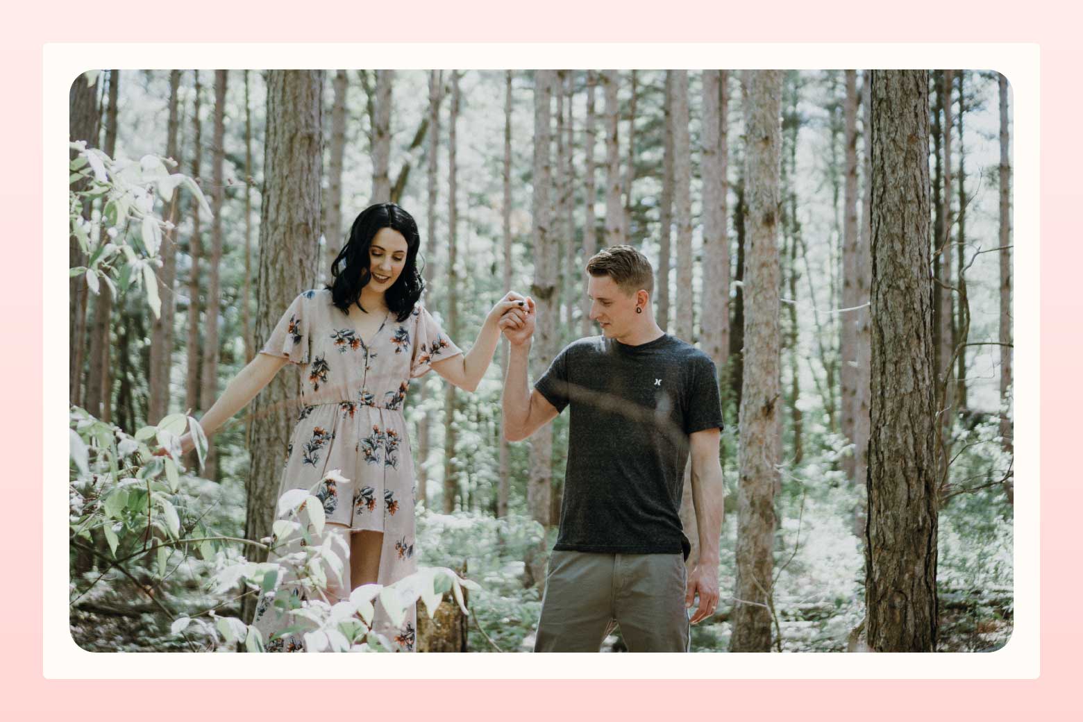 Man holding the hand of his fiancee as she walks along a fallen tree in the forest