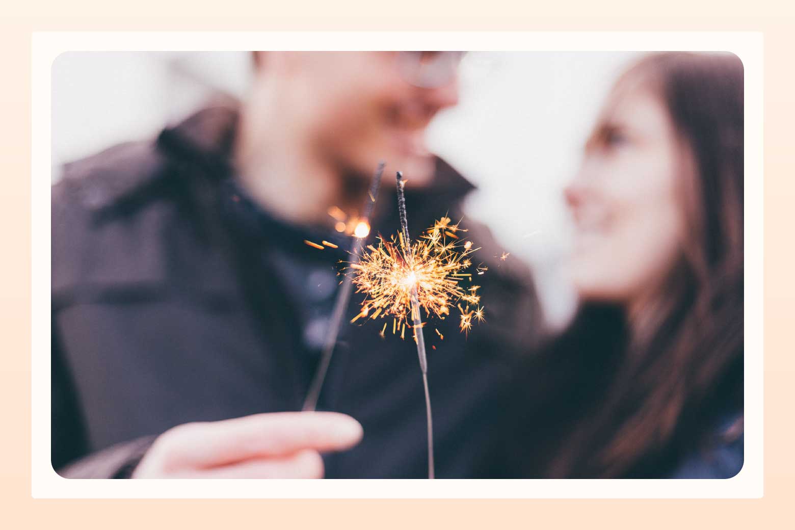 Close up on sparklers in foreground with a blurry smiling couple looking at one another in the background