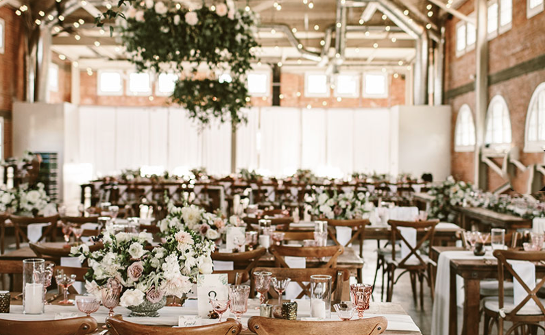 indoor wedding reception setup with flowers, wood chairs, and white drapes at brick venue in san diego