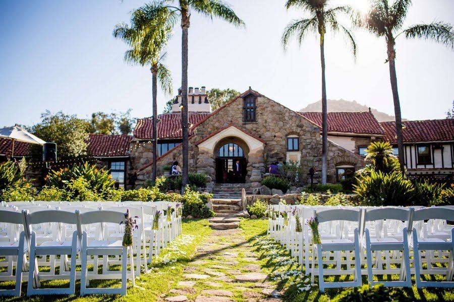 outdoor wedding ceremony setup with white chairs in front of palm trees at mt. woodson castle in san diego