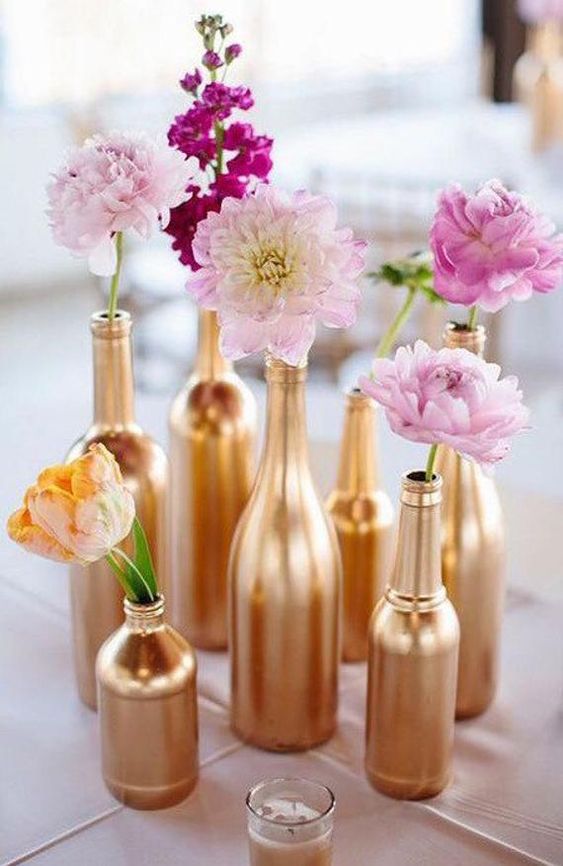painted gold bottles filled with pink flowers on a table