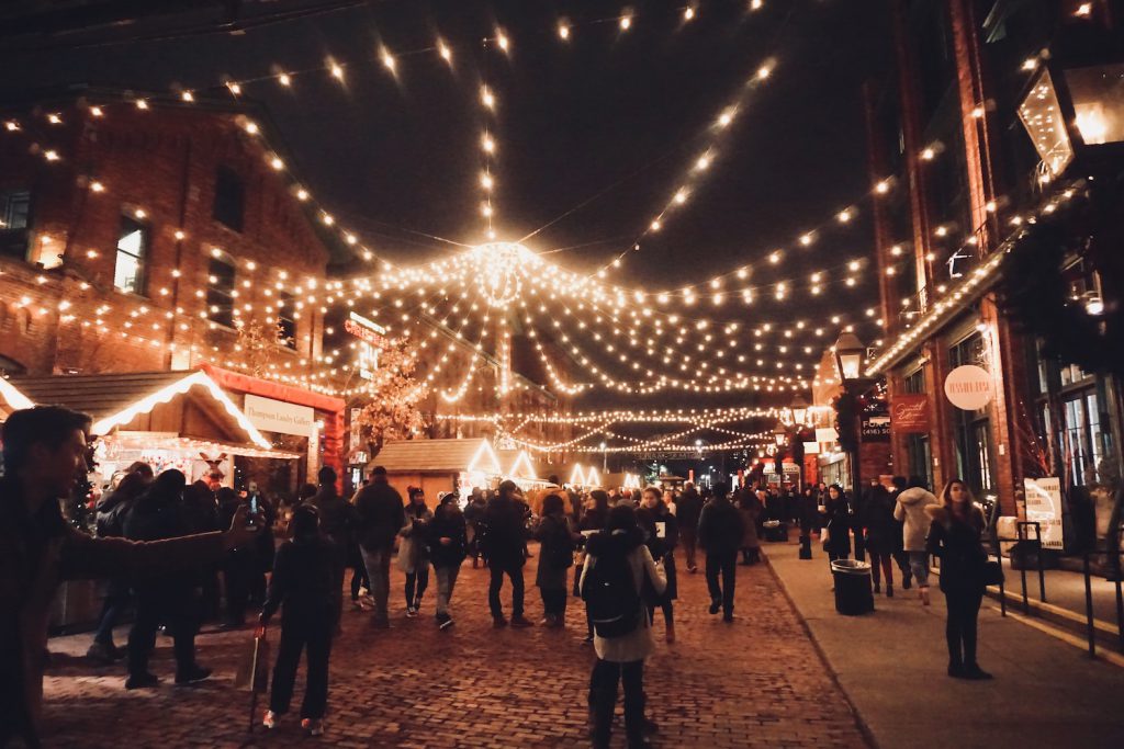 people gather at night under festive twinkle lights at the toronto christmas market
