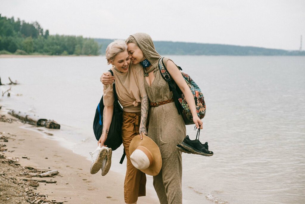 A backpacking couple on their honeymoon walking on the beach holding their shoes