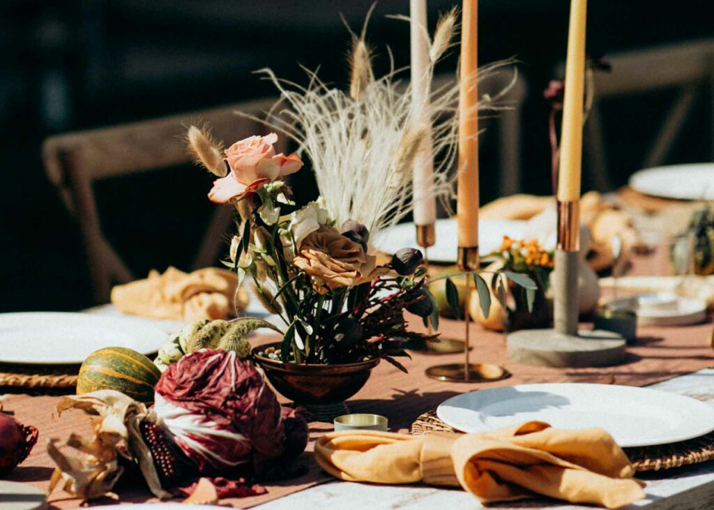 Fall harvest centerpiece with a deep purple corn husk, cabbage, gourds, taper candles and a floral centerpiece with feathers