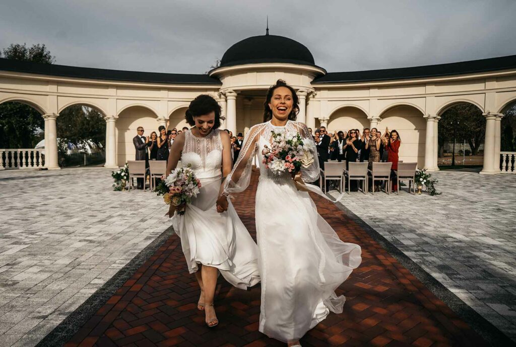 same-sex bridal couple running together down wedding aisle