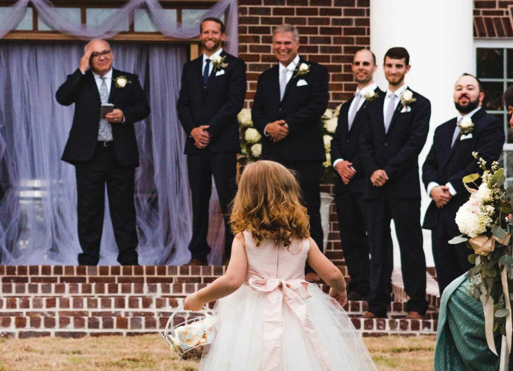 flower girl walking down the aisle in front of groom and groomsmen