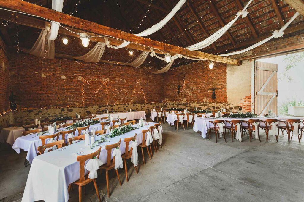 White fabric is draped from the ceiling. Twinkle lights contrast against exposed brick walls. White linens on reception tables are topped with greenery and candles.