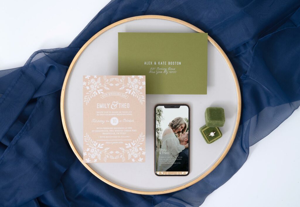 Wedding invitation guide photo featuring Joy's Rustic Floral theme with an invitation, envelope, mobile website and ring on a plate