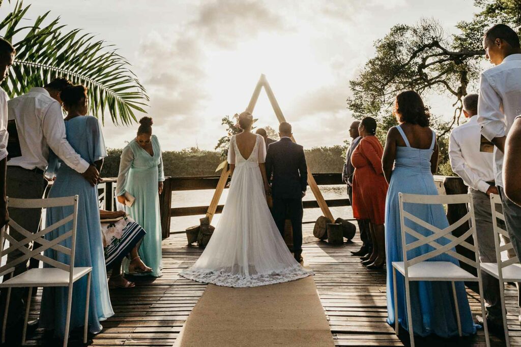 A woman in a wedding dress and a man in a suit standing at a triangle-shaped altar with wedding guests looking on