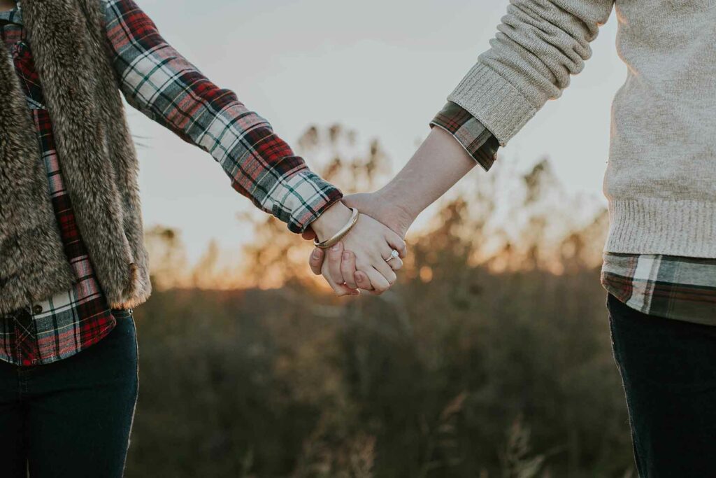 What to Wear in Engagement Photos: A woman wearing flannel and a faux fur vest holding hands with another woman wearing a sweater layered over flannel