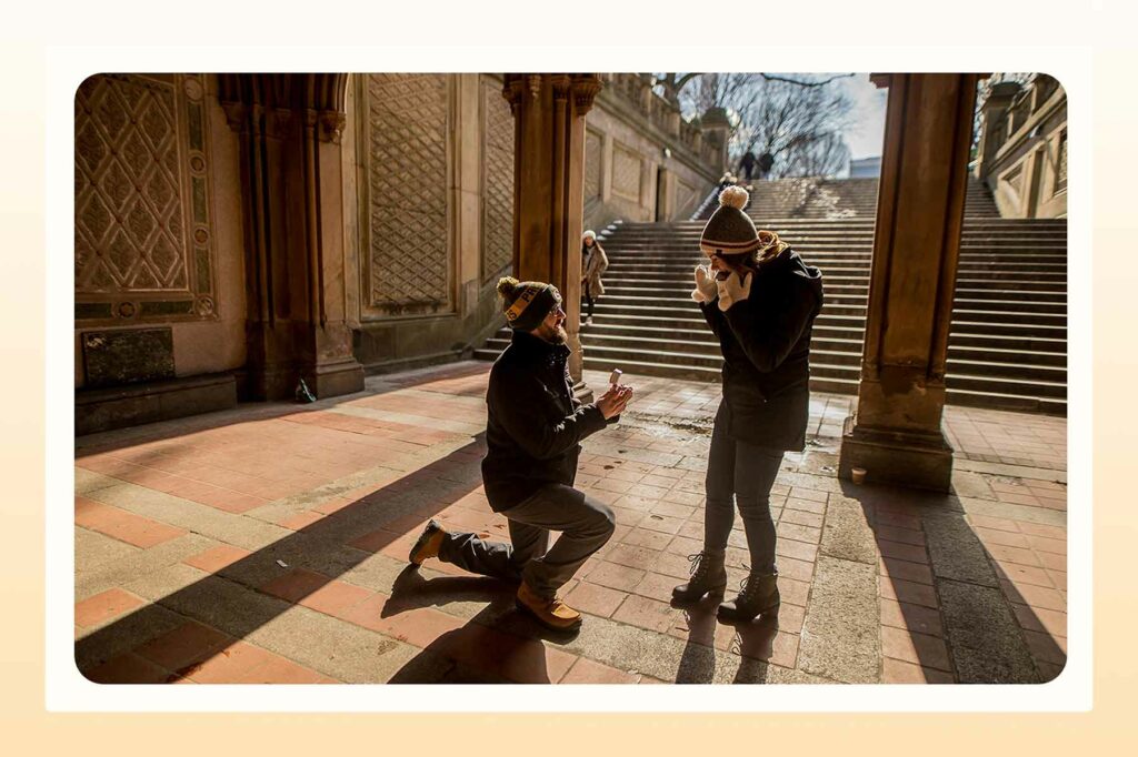 A man kneeling at the foot of steps and a happy woman smiling with her hands by her face in surprise