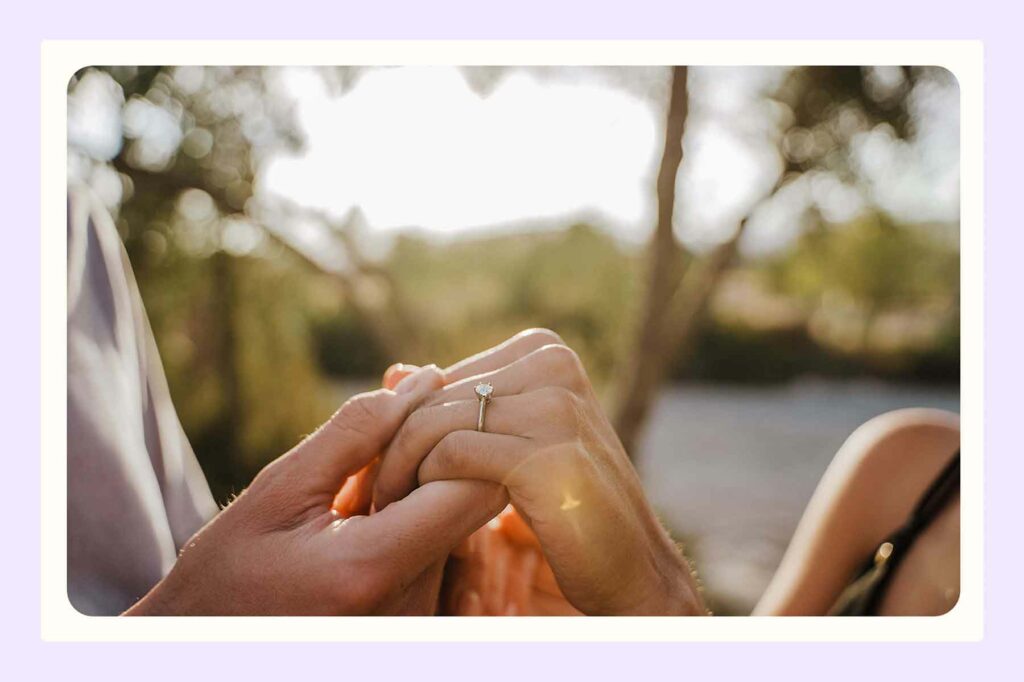 A closeup of two hands, with one wearing an engagement ring on their ring finger