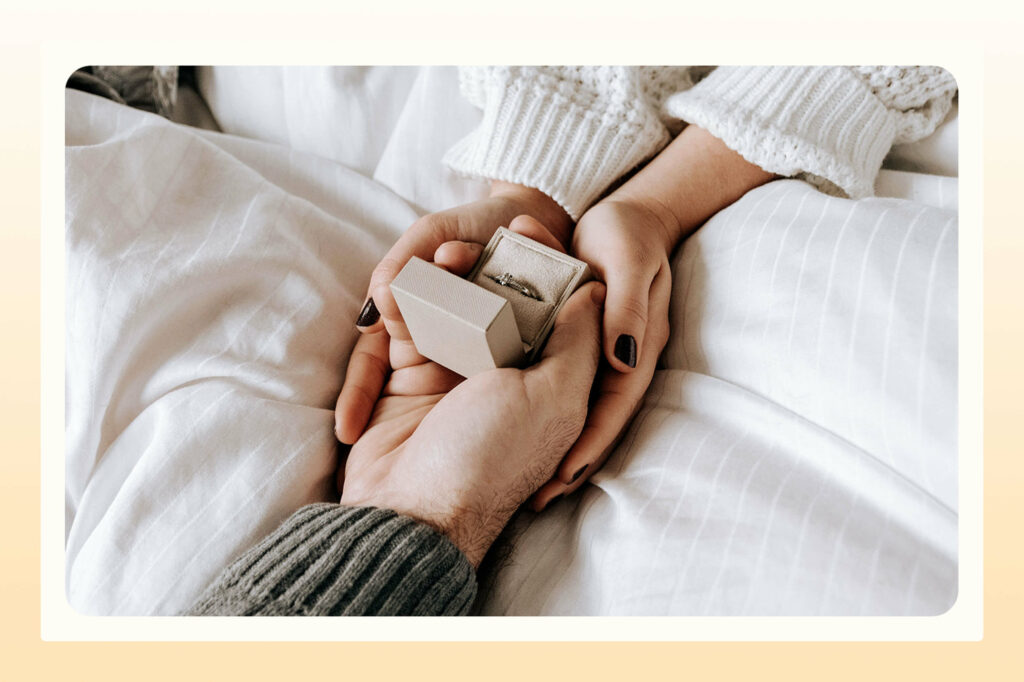 an outstretched hand holding an open engagement ring box and another set of hands holding it